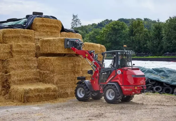 Chargeuse articlée compact électrique Hoftrac de Weidemann devant un tas de bottes de paille.