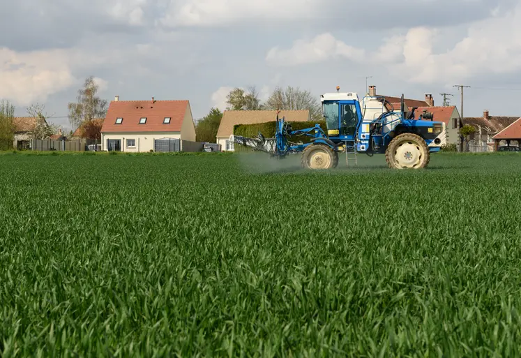 un trcateur épand des pestices dans un cham près de maisons
