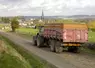 Tracteur tirant une benne agricole laissant de la boue sur une route de campagne