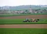 Tracteur fertilisant un champ devant un village 