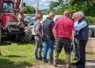 un groupe de personnes discutent devant un  tracteur où sont pendues deux carcasses de mouton