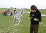 Homme nettoyant une buse dans un champ, machine agricole en arrière-plan