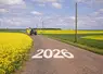  Tracteur sur une route de campagne entourée de champs de colza avec l’inscription 2026 sur la route.  