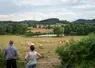 Agriculteurs observant leurs bovins près d'un étang dans un paysage bocager.