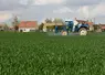 un trcateur épand des pestices dans un cham près de maisons