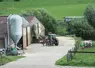 Cour de ferme avec bâtiment visible, un bovin dans une prairie et un tracteur.