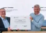 deux hommes assis montrent à l'objectidf un document