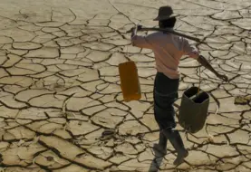 homme transportant sur ses épaules des récipients d'eau et qui marche sur un sol craquelé