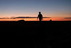 Silhouette d'une personne debout dans un champ avec un coucher de soleil. 