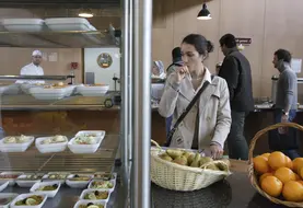 Etudiante avec son plateau dans une cantine scolaire en réflexion sur son menu, devant des fruits et des entrées. 