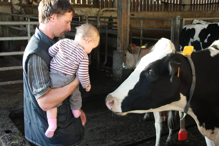 Un agriculteur avec son enfant dans les bras devant une vache laitière