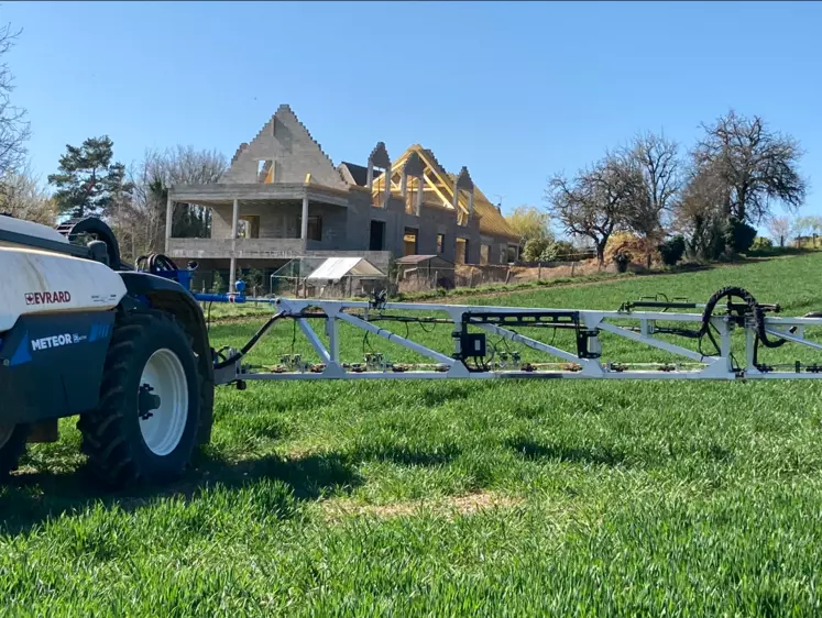 Pulvérisateur dans un champ avec maison en construction à l'arrière