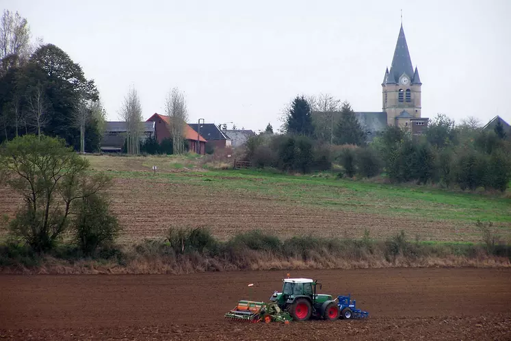 Tracteur semant du  blé à l'autome devant un village.