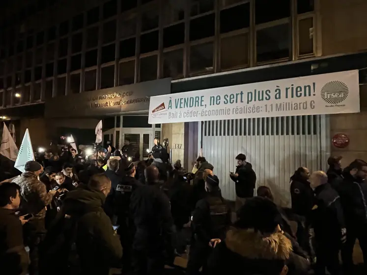 Des agriculteurs au petit matin devant l'Inrae sous une banderole avec l'inscription "à vendre, ne sert plus à rien"