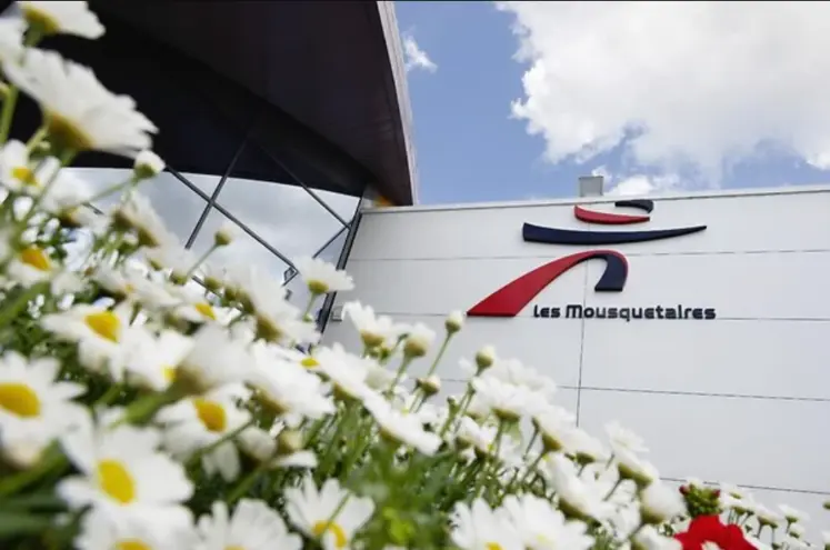 logo les mousquetaires sur un mur blanc avec fleurs en premier plan