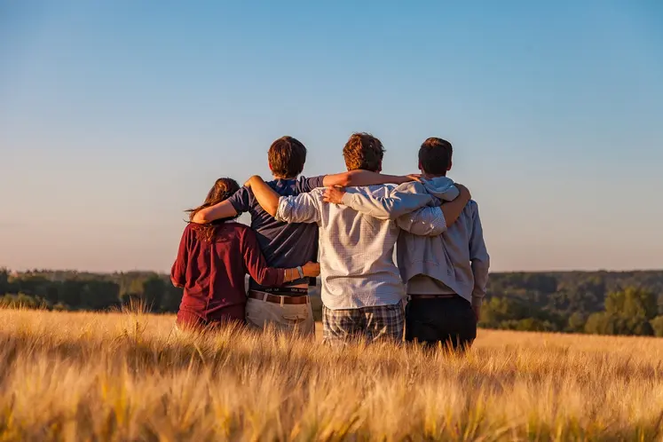 Quatre jeunes de dos se tenant par les épaules au milieu d'un champ.