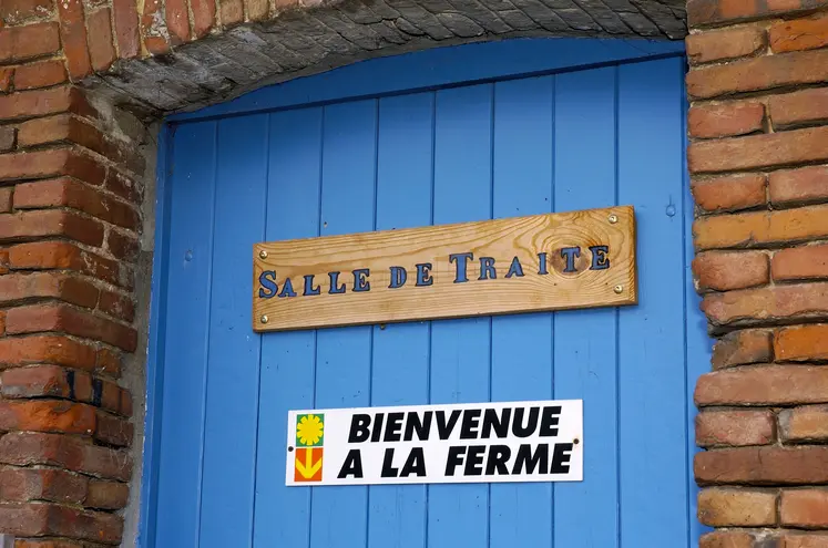 panneau bienvenue à la ferme sur une porte bleue en dessous d'un autre panneau mentionnant salle de traite