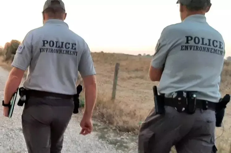 Deux agents de l'OFB avec l'inscription police de l'environnement dans le dos dans un chemin entre des parcelles agricoles.