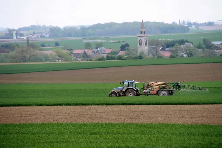 Tracteur fertilisant un champ devant un village 