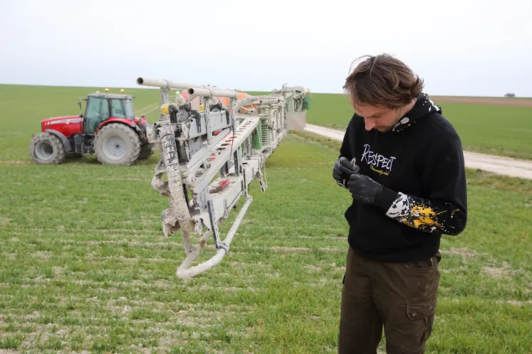 Homme nettoyant une buse dans un champ, machine agricole en arrière-plan