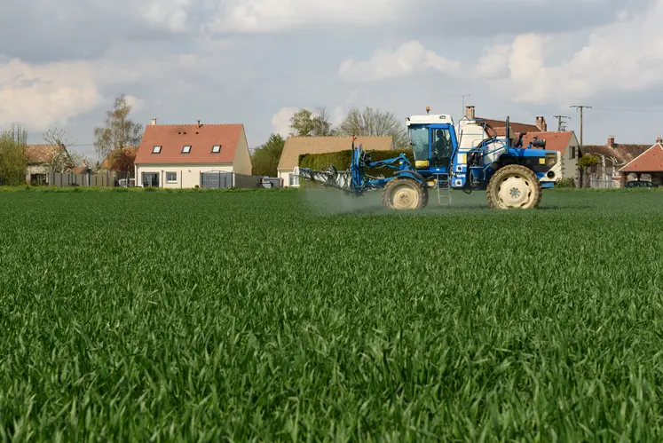 Tracteur épandant des pesticides dans un champ, maisons en arrière-plan