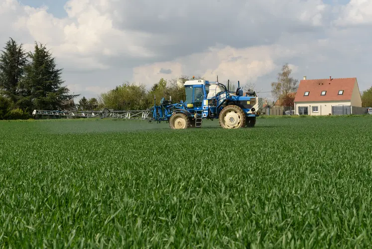 au premier plan un tracteur utilisant des pesticides et en arrière plan une maison