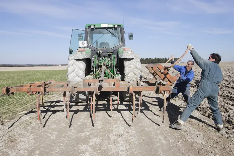 Deux agriculteurs mettant en place une herse de 4 mètres pour préparer les bords de champs
