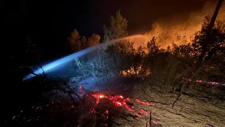 Lance à eau ciblant les flammes et les braises en soirée lors de l'incendie historique ayant touché l'Aude depuis le 5 août.