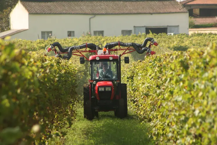 Une agricultrice dans son tracteur traite des pieds de vignes grâce à des pulvérisateurs.