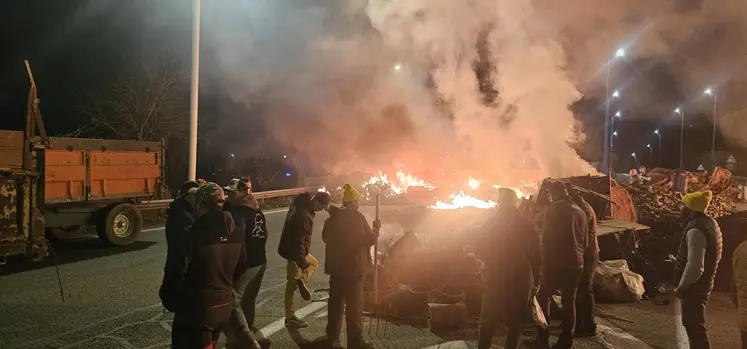 Blocage d'une voie d'autoroute le soir par des agriculteurs de la Coordination rurale, avec des pneus enflammés, des palettes de bois et des ballots de paille. 