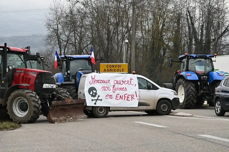 Tracteurs bloquant une route, avec une banderole sur une voiture "Mercosur ouvert, nos fermes en enfer"