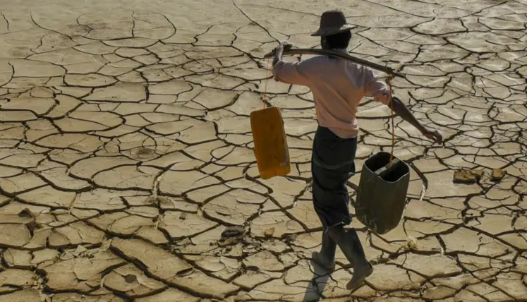 homme transportant sur ses épaules des récipients d'eau et qui marche sur un sol craquelé