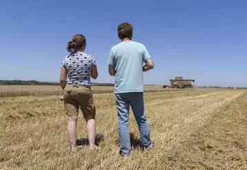 Un agriculteur et sa fille dans un champ avec moissonneuse batteuse au loin.