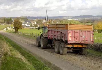 Tracteur tirant une benne agricole laissant de la boue sur une route de campagne