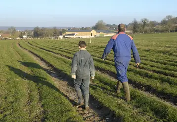 Un homme et un enfant en tenue d'agriculteur marchent dans un champ