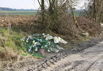 Déchets près d'un terrain agricole. On voit des bouteille en verre. 