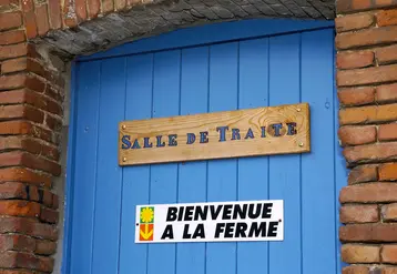 panneau bienvenue à la ferme sur une porte bleue en dessous d'un autre panneau mentionnant salle de traite