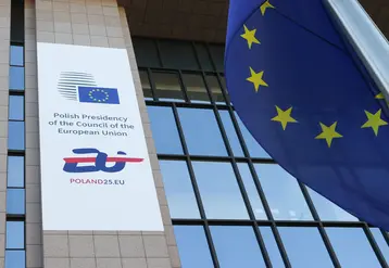 Bannière de la présidence polonaise du Conseil de l'UE sur une partie du bâtiment du Conseil à Bruxelles, avec un drapeau européen au premier plan.  