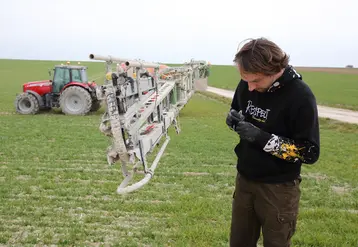 Homme nettoyant une buse dans un champ, machine agricole en arrière-plan