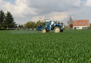 au premier plan un tracteur utilisant des pesticides et en arrière plan une maison