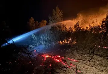 Lance à eau ciblant les flammes et les braises en soirée lors de l'incendie historique ayant touché l'Aude depuis le 5 août.