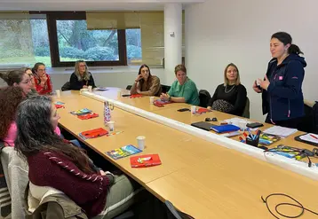 des femmes assises autour d'un bureau et une femme debout