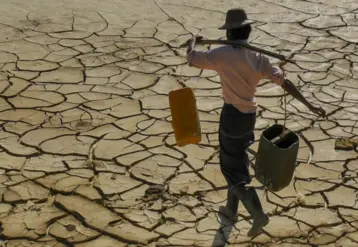 homme transportant sur ses épaules des récipients d'eau et qui marche sur un sol craquelé