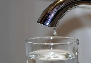 robinet avec une goutte d'eau dans un verre déjà presque rempli