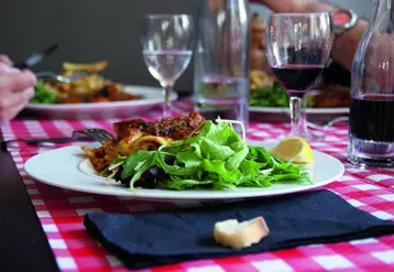 Table de restaurant avec un focus sur une assiette et du vin rouge. 
