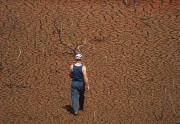 homme de dos marchant sur un sol désséché et craquelé