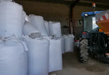 des sacs d'engrais et un tracteur entreposés dans un hangar agricole