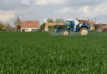 un trcateur épand des pestices dans un cham près de maisons