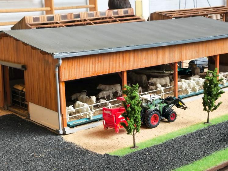 Un tracteur Fendt équipé d'un chargeur frontal, attelé à une pailleuse de couleur rouge de la marque Jeantil. L'ensemble a été mis en scène l'année dernière devant un bâtiment d'élevage abritant un troupeau de bovins de race charolaise.