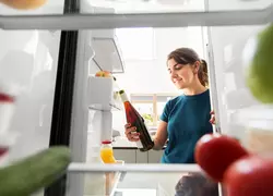 healthy eating, food and diet concept - happy woman taking orange wine bottle from fridge at home kitchen